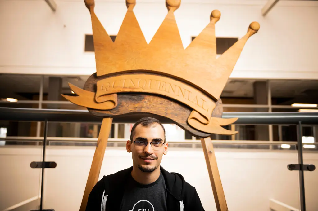 Artem Skitenko sits beneath a large carved wooden crown that reads Quinquennial