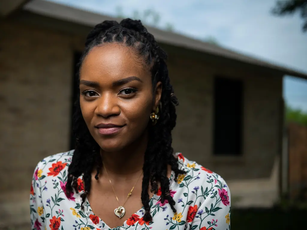 Asha King in a floral blouse stands in front of her brick home