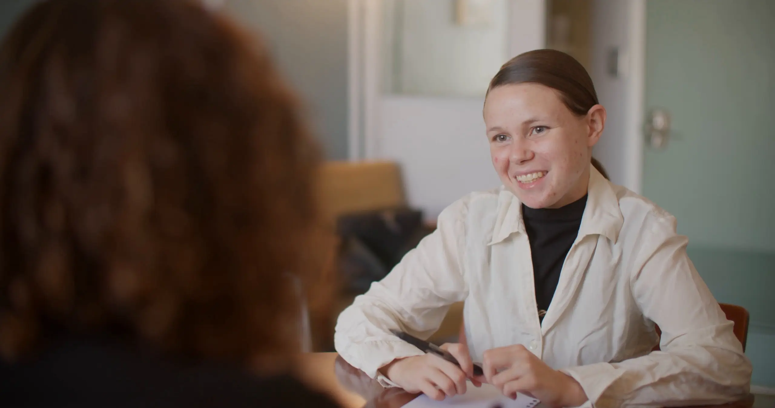 Ashley Keen smiles with a pen in hand at a meeting table across from a woman, in her SAMMinistries Journeys of Hope story.