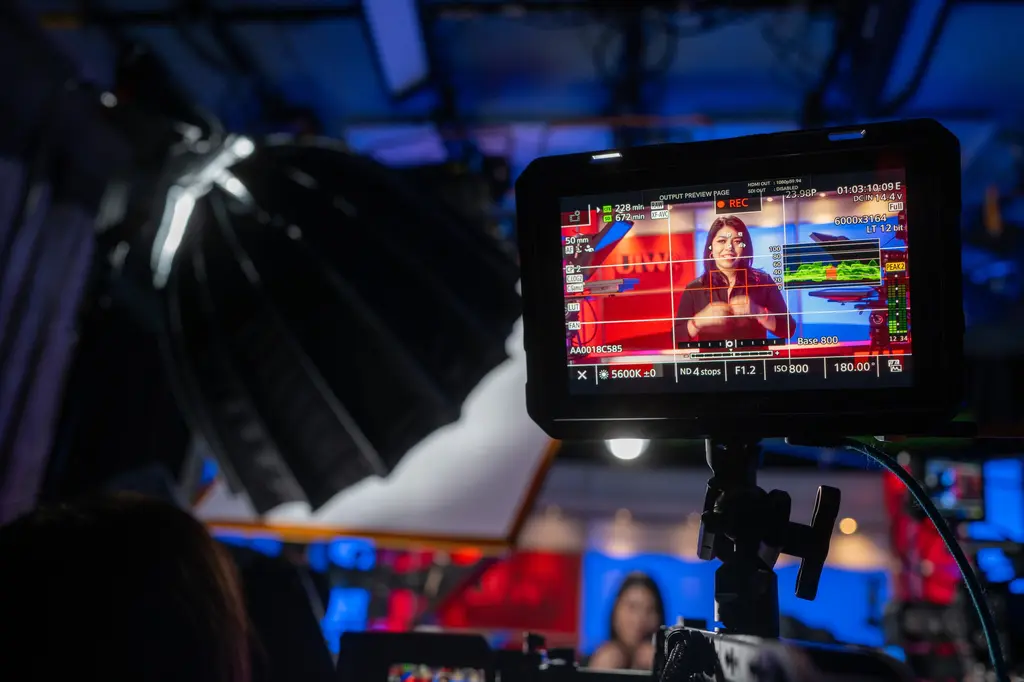 Un monitor montado en la cámara muestra a Isabel Lara en un set de televisión rojo y azul de UIW, con un softbox grande arriba.