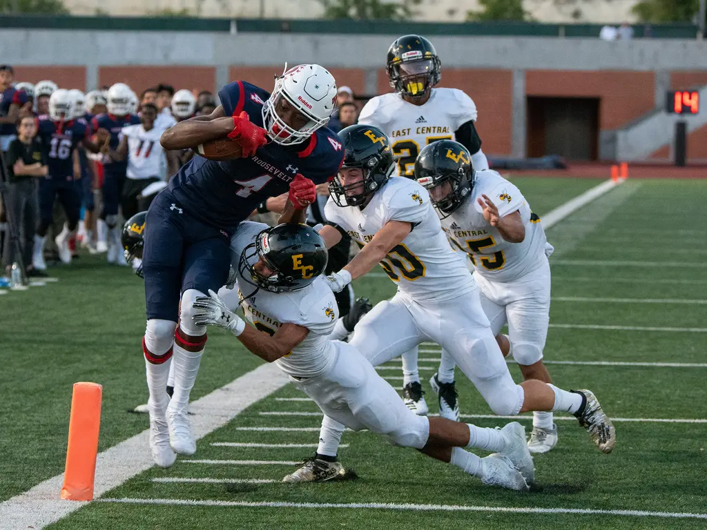 A Roosevelt receiver in a navy No. 4 jersey dives for the pylon as East Central defenders in white grab at him.