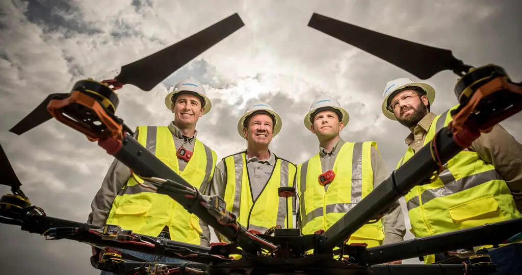 A DataWing Global crew in hard hats and safety vests stands behind the rotor arms of a large drone