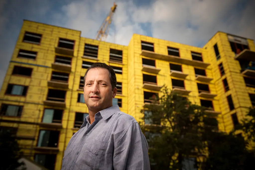 David Adelman stands in front of a yellow apartment building under construction, a crane above it