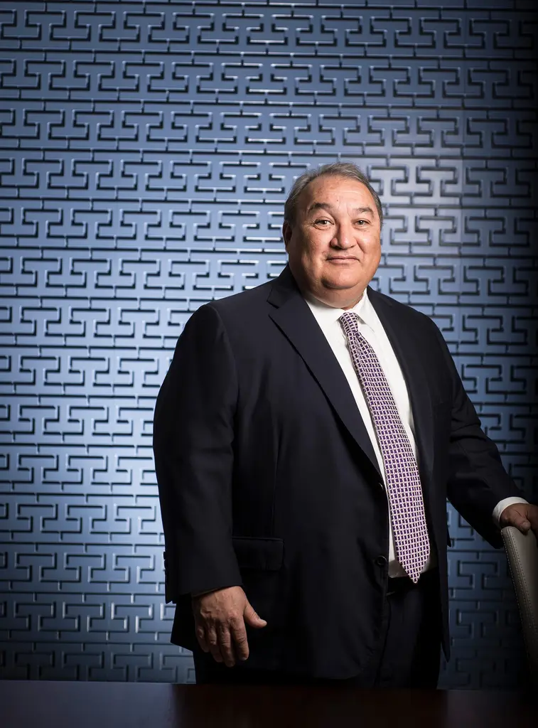 Edward Valdespino in a dark suit and patterned tie stands before a blue geometric wall