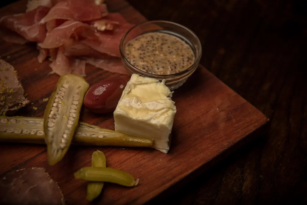 A wedge of soft cheese, an olive and pickled okra beside a dish of whole grain mustard.