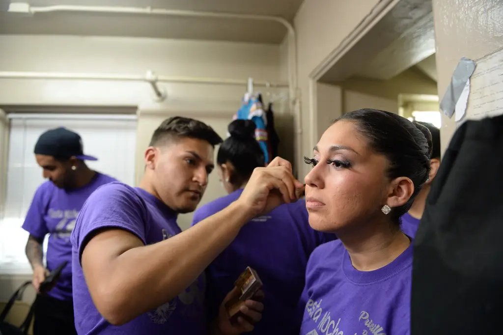 A young man in a purple T-shirt adjusts a woman’s eyelashes as she sits still with her eyes half closed.