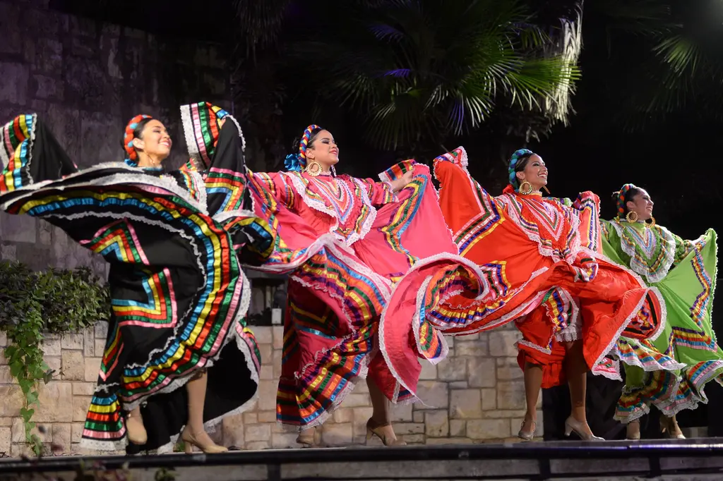 Four dancers in black, pink, red and green folklorico dresses spread their ruffled skirts wide as they dance on the stone stage.
