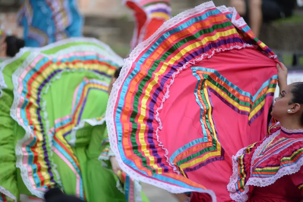 Close view of bright pink and green ruffled skirts with ribbon stripes swirling as dancers spin.