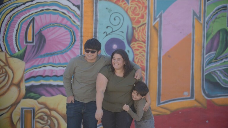 NPower alum Geneva Knott smiles as two boys hug her in front of a colorful sugar skull mural.