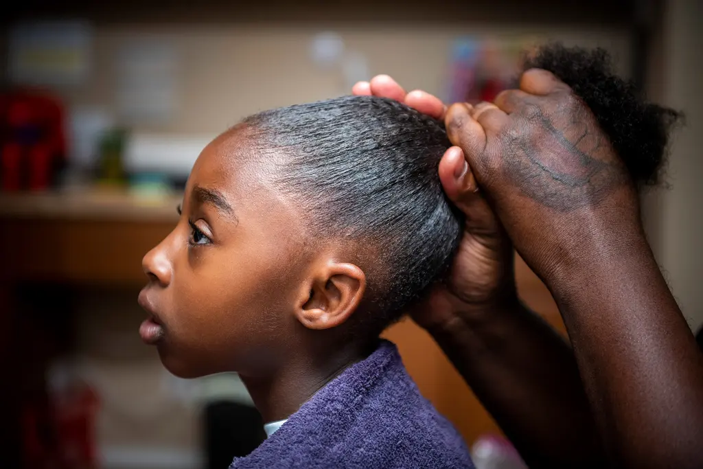 A close view of a girl in profile as her father's hands gather her hair into a ponytail.