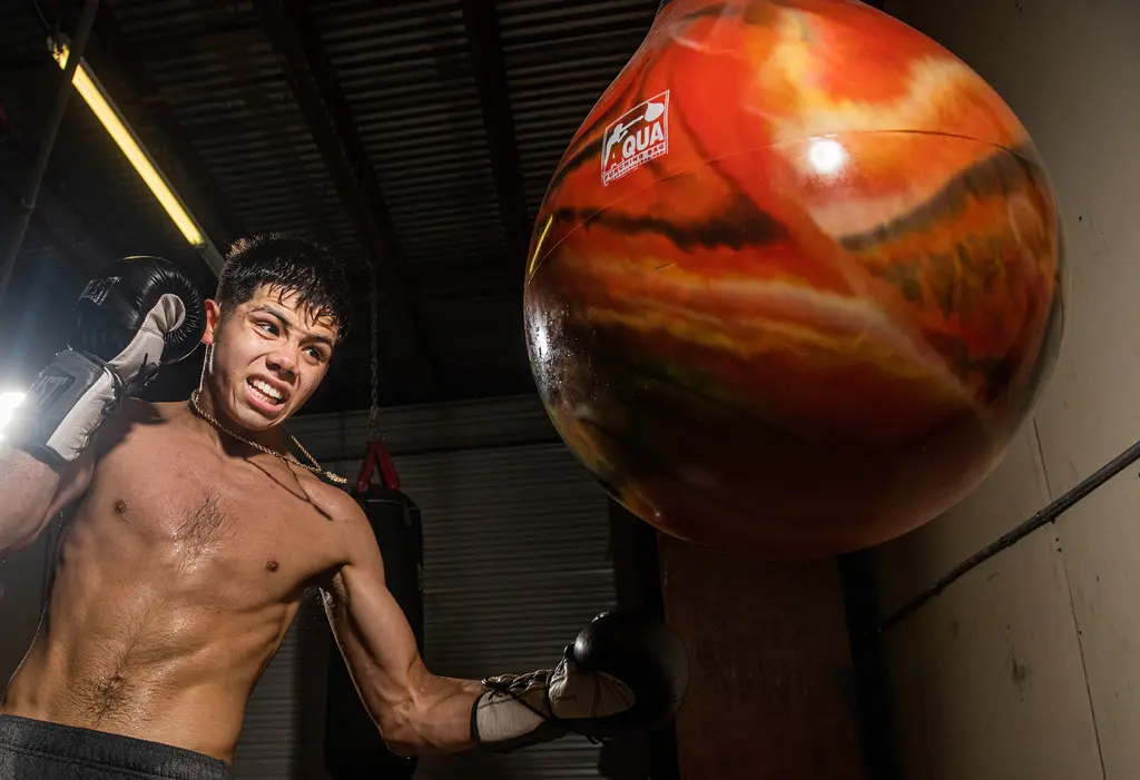 A young boxer grimaces as he punches a swinging orange water bag.