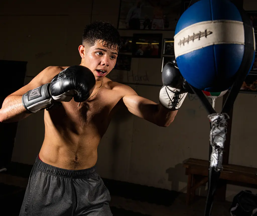 A shirtless young boxer punches a blue and white double-end bag.