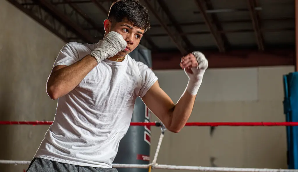 A young boxer in a white T-shirt and hand wraps throws a punch in the ring.