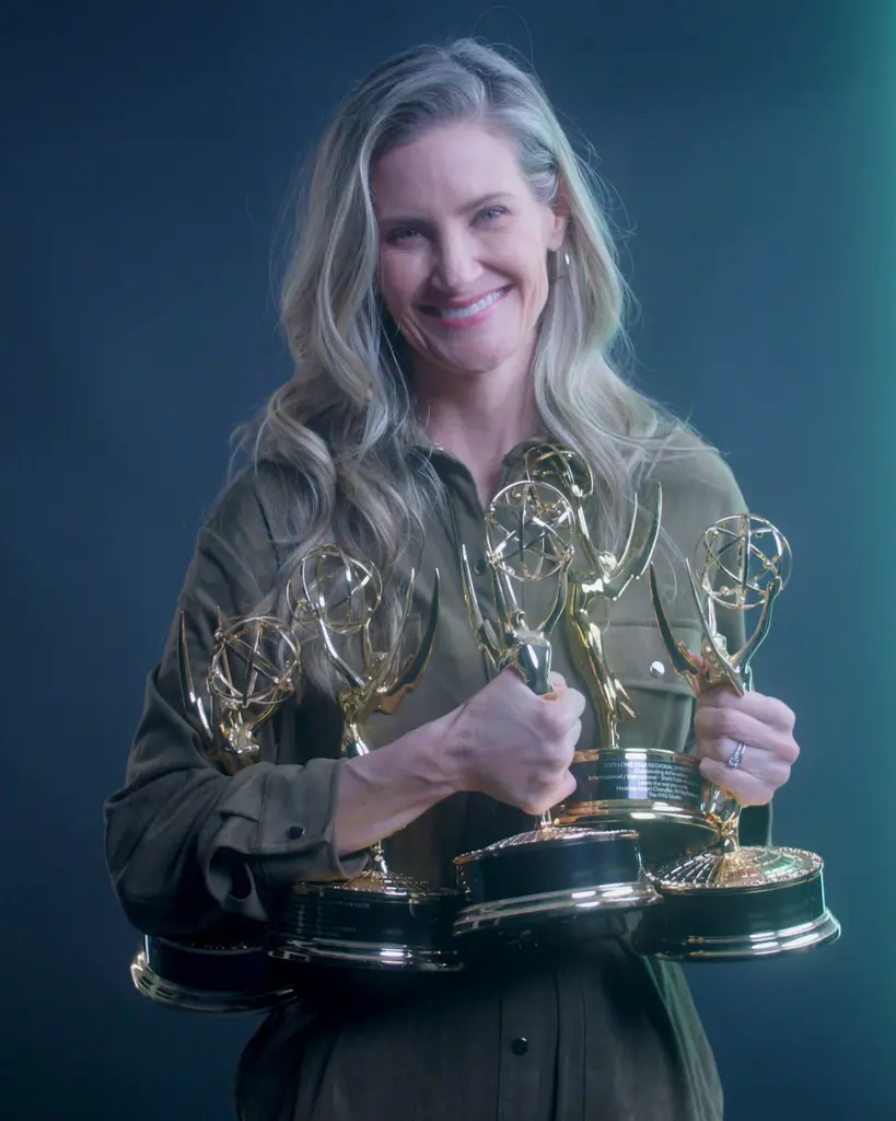 Heather Angel Chandler, CEO and founder of IMG Studio, smiles as she holds an armful of Emmy statuettes against a dark backdrop.
