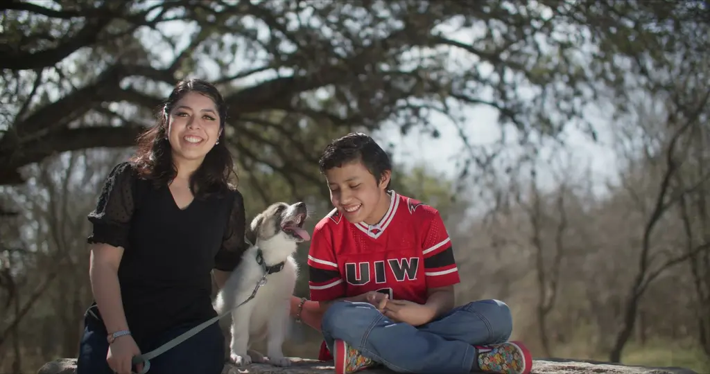 Isabel Lara smiles beside Max and a puppy under the trees in her SAMMinistries Journeys of Hope story.