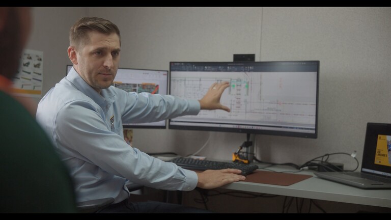 Ben Emery, a JCB senior engineering project manager and former apprentice, points to a floor plan on his monitor as he talks with an apprentice.
