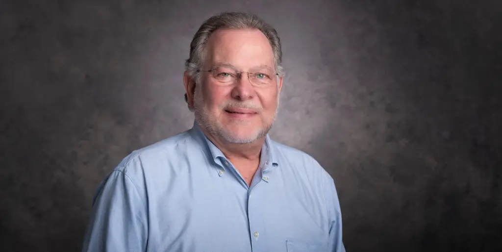The Joeris CEO in glasses and a light blue button-down shirt, against a gray studio backdrop.