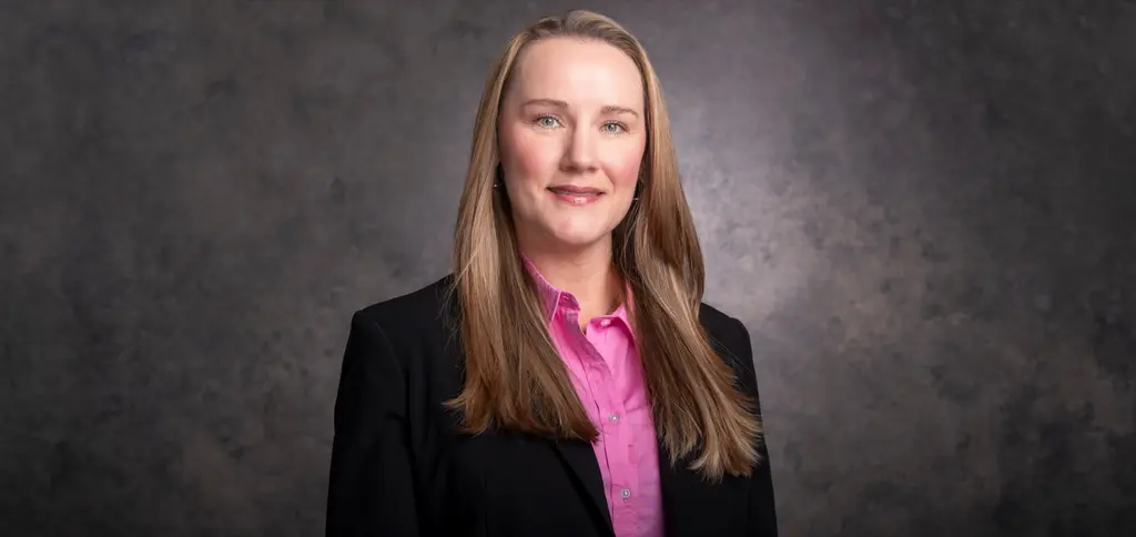 A smiling Joeris executive with long hair, in a black blazer and pink shirt, against a gray studio backdrop.