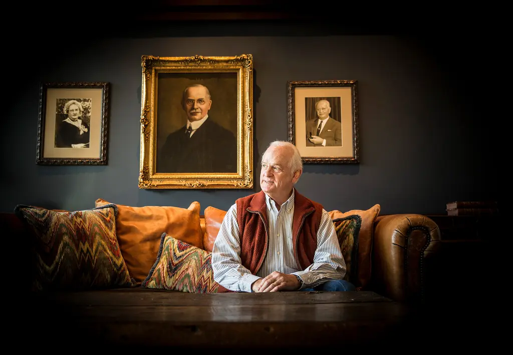 Kit Goldsbury in a red vest sits on a leather sofa beneath framed historic portraits