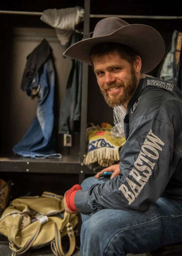 Lucas Creasy, in a cowboy hat and a Barstow rodeo jacket, smiles as he sits beside his locker.