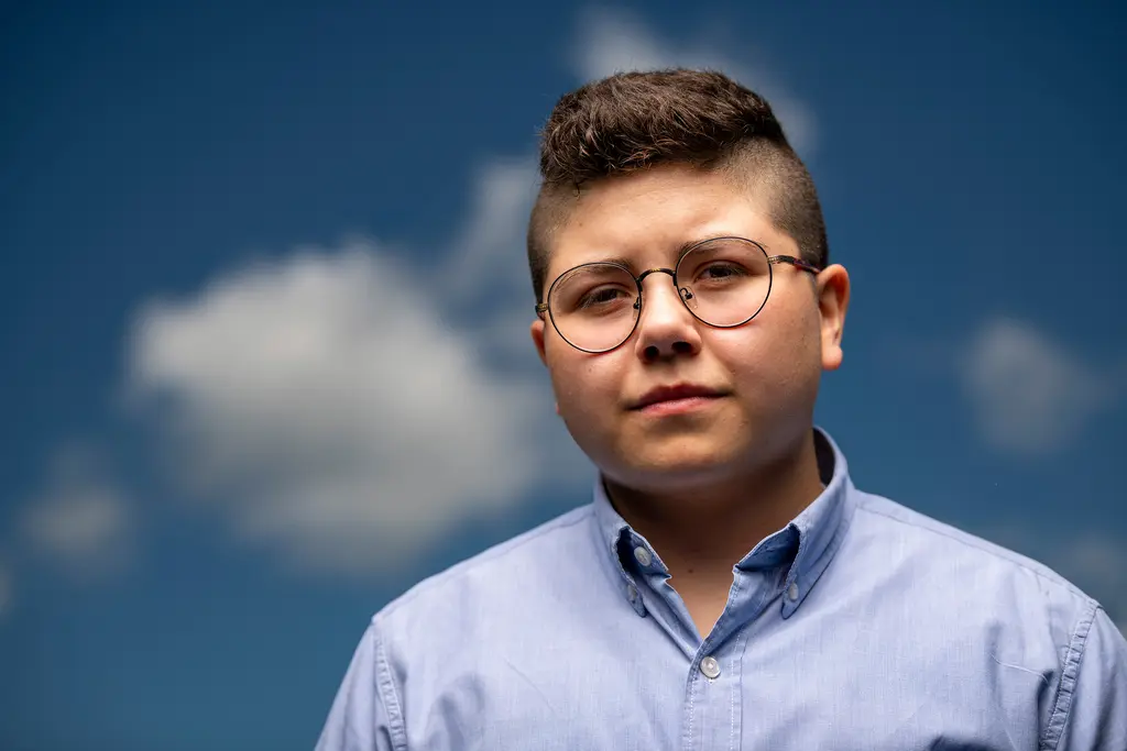 Map Pesqueira in round glasses and a light blue shirt stands against a blue sky with clouds