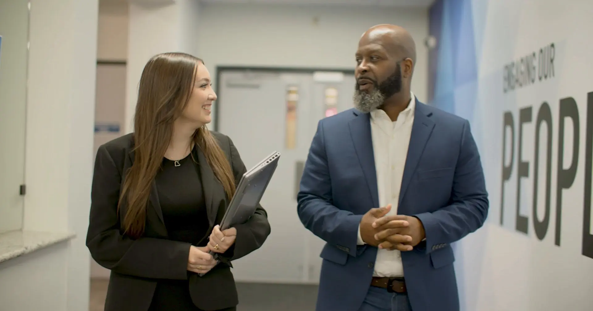 Estrella Davila, a data analyst at Accenture Federal Services and an NPower alum, talks with Quincy Harper, the company's military recruiting lead, as they walk down an office hallway.