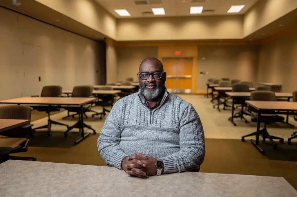 Byron J. Cooper, in a gray sweater and glasses, sits at a table in an empty meeting room.