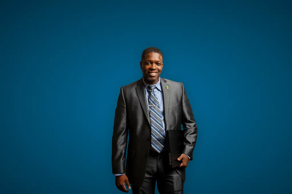 Raymond Robinson, Jr., in a gray suit and striped tie, stands against a blue backdrop.