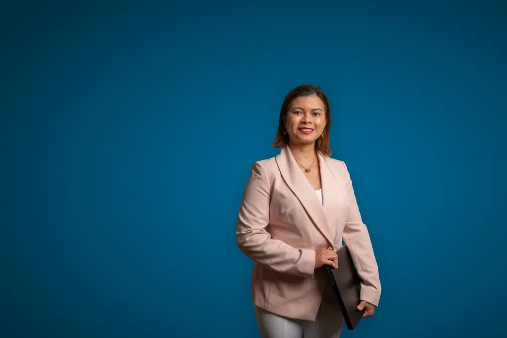 Zooey Nguyen, in a pink blazer, holds a laptop against a blue backdrop.