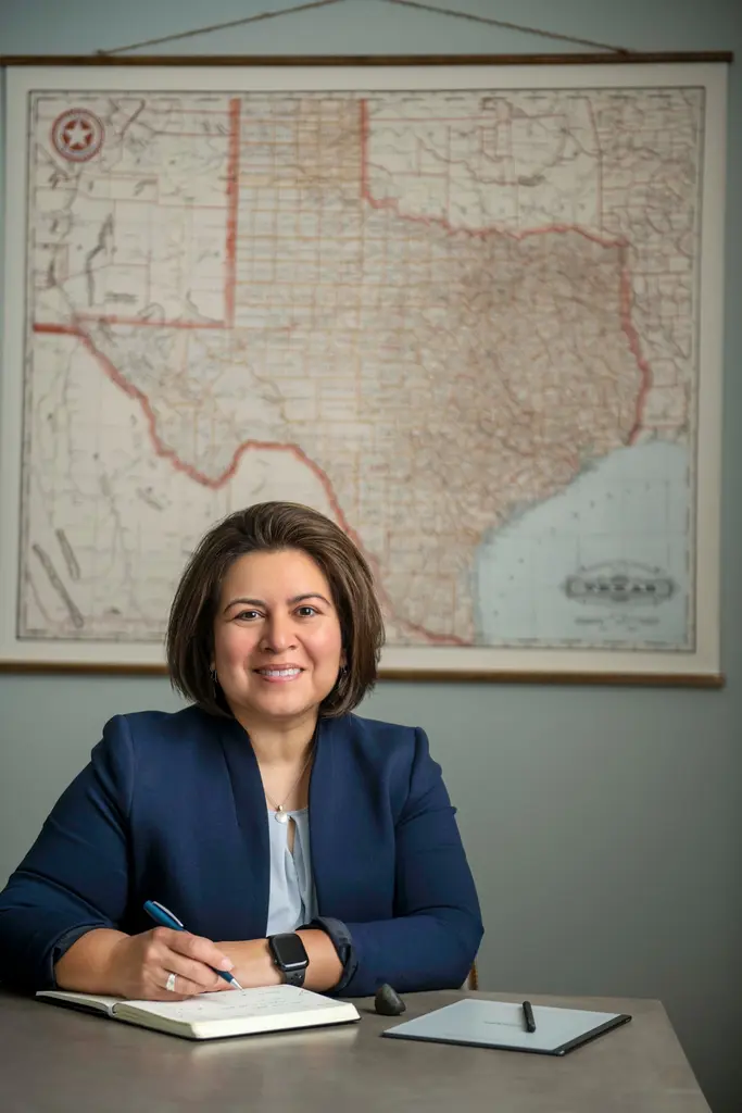The same woman smiles as she writes in a notebook at a desk, beneath a vintage map of Texas.