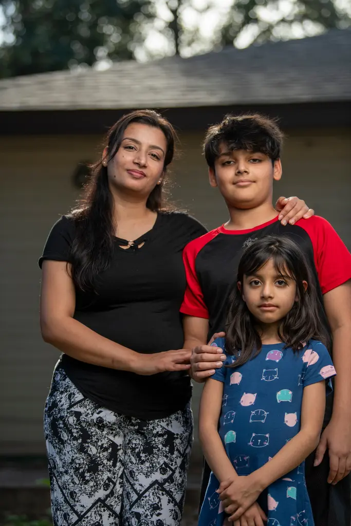 Anju Kumari stands outside a house with her son, in a red and black shirt, and her daughter, in a blue print dress.