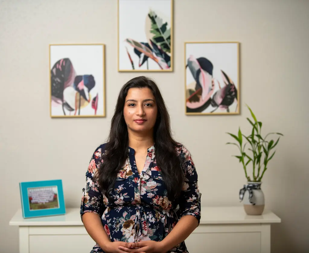 Anju Kumari, in a floral dress, sits in front of three framed plant prints and a potted bamboo plant.