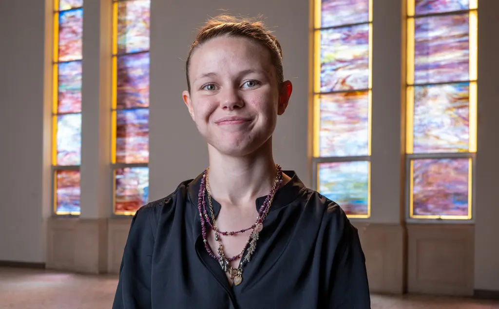 Ashley Keen smiles toward the camera in front of tall stained-glass windows.