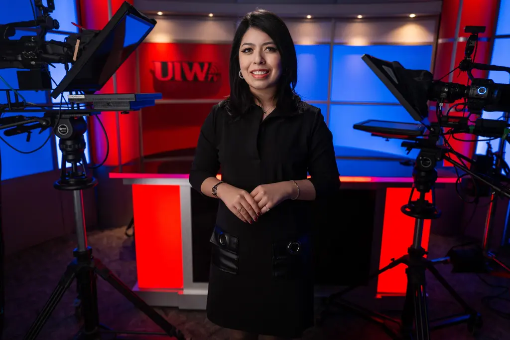 Isabel Lara, in a black dress, stands on the UIWtv studio set.