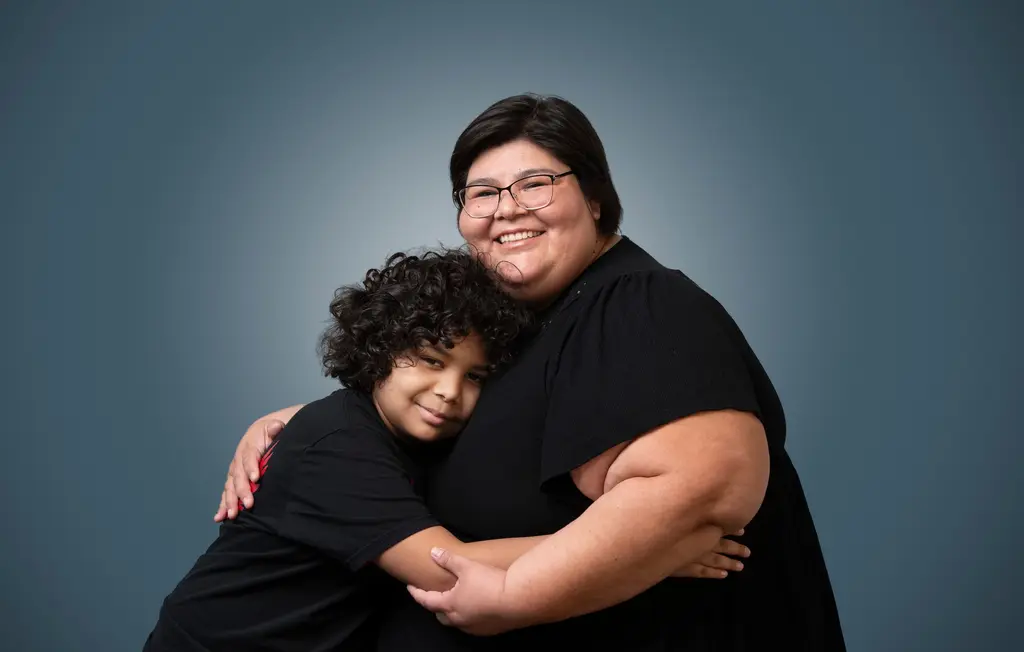 Libby Rippetoe and her son hug and smile against a slate-blue backdrop.