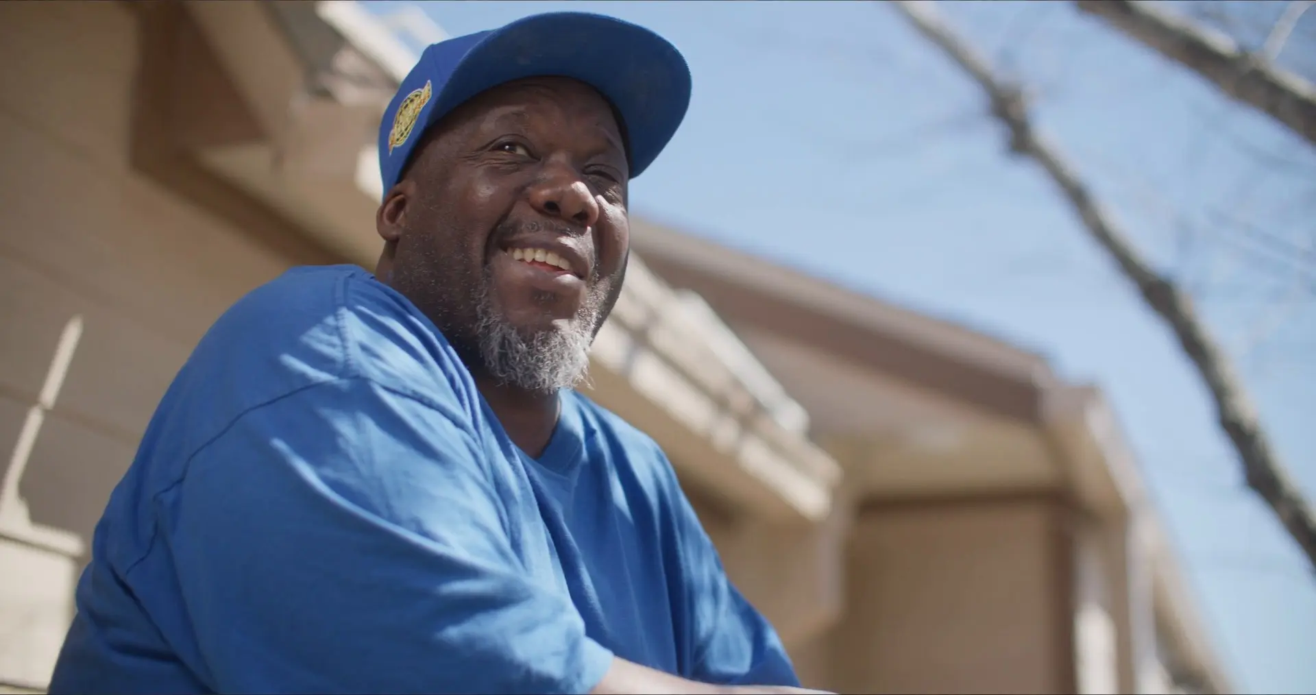 Scott Washington, in a blue cap and blue T-shirt, laughs as he looks up outside his apartment building in his SAMMinistries Journeys of Hope story.