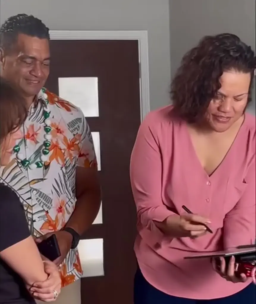Sorepa Gallahar, con blusa rosa, firma su autorización en una tableta con un lápiz digital mientras su esposo, Tas Gallahar, con camisa floreada y collar, sonríe a su lado.