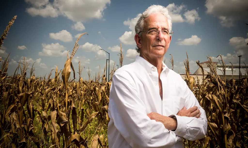 William Ochse in a white shirt stands with his arms crossed in front of a field of dry corn
